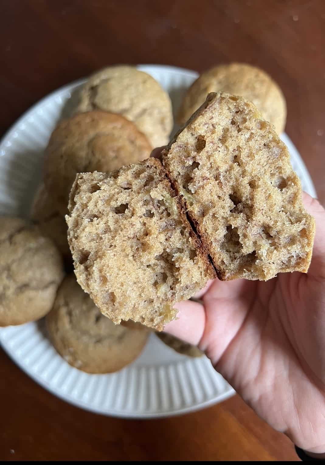 a banana muffin split in half in front of a white plate